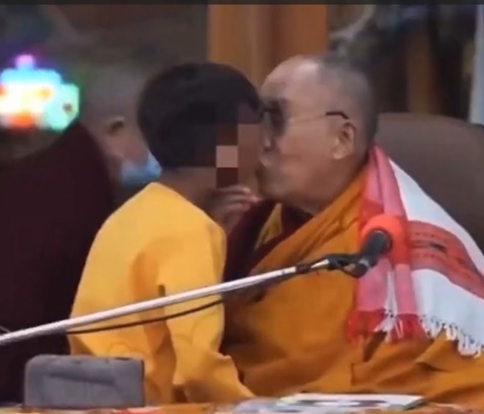 mas Dalai Lama, de 87 anos, mostrando os lábios pedindo um beijo, e puxa o menino pelo queixo para beija-lo, colocando a língua para fora e pedindo a criança para chupa-lá.