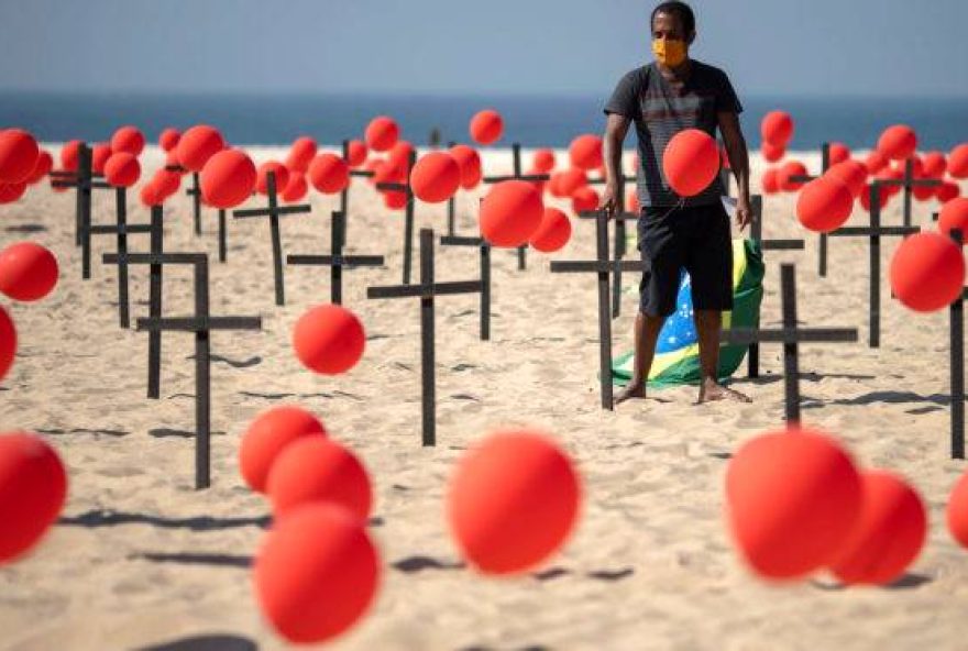 Brazilian Marcio Antonio do Nascimento, father of 25-year-old Hugo do Nascimento, who died from the new coronavirus, holds a Brazilian flag beside crosses before a thousand red balloons are released, during a tribute to COVID-19 victims organized by the Rio de Paz NGO at the Copacabana beach in Rio de Janeiro, Brazil, on August 08, 2020. (Photo by Mauro Pimentel / AFP)