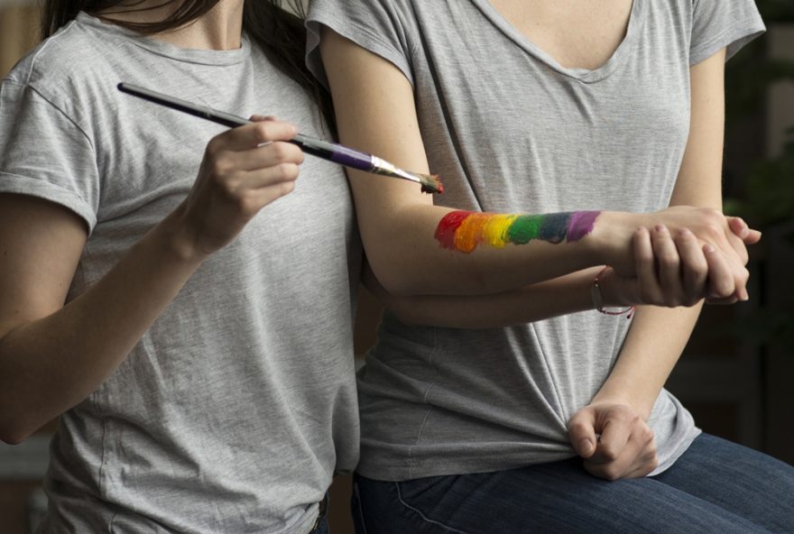 9f18239d-linda-mulher-lesbica-pintando-bandeira-de-arco-iris-na-mao-da-namorada-com-pincel