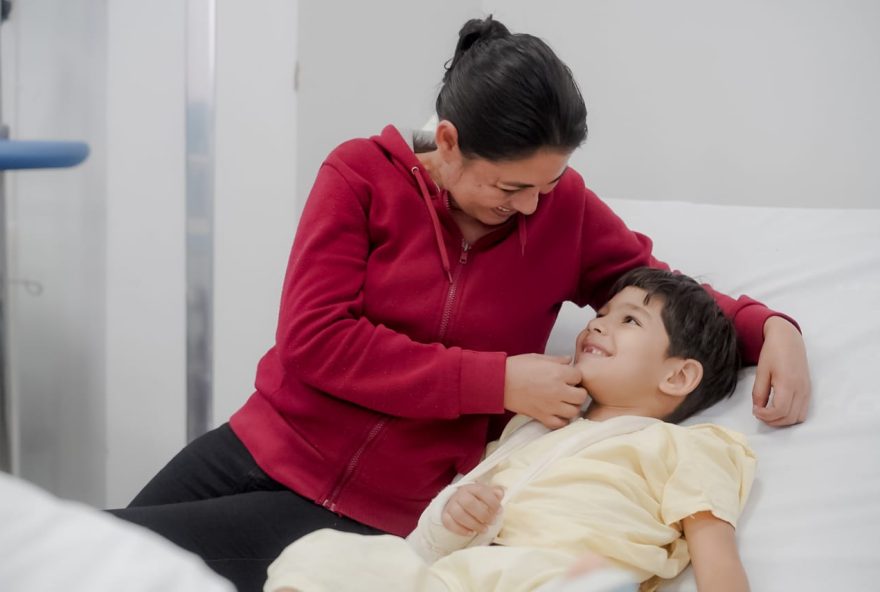 Com a mãe, Lúcia, o pequeno Heitor sorri, em leito do Hecad, após cirurgia bem-sucedida no braço direito (Foto: Iron Braz/SES)