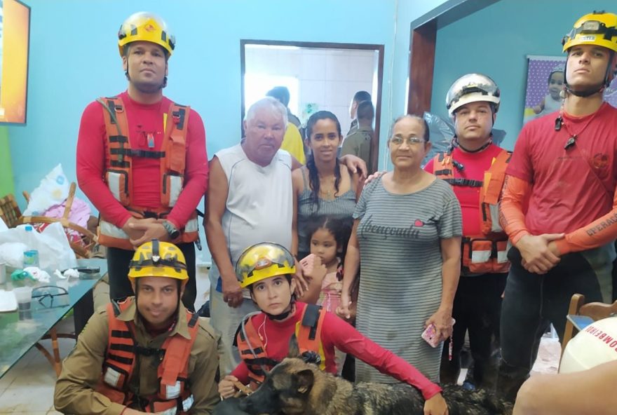 Dona Maria Aparecida, de vestido, ao lado do marido, da neta e bisneta, com  bombeiros militares. (Foto: Arquivo Pessoal/Maria Aparecida)