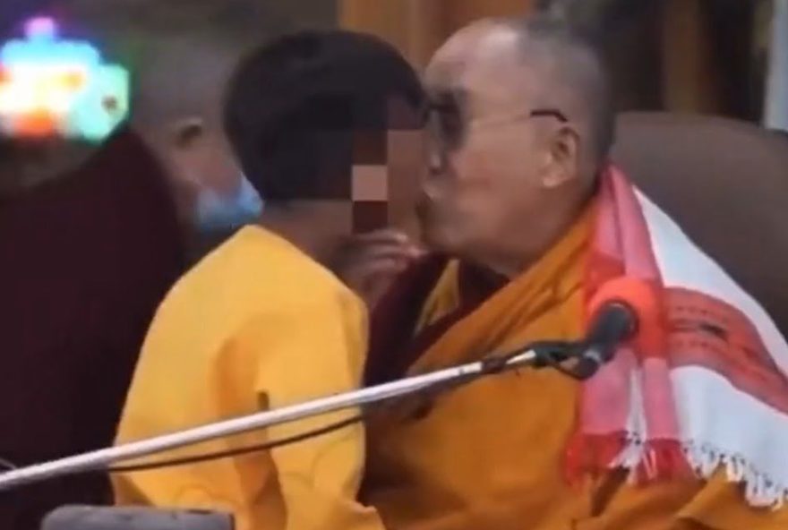 mas Dalai Lama, de 87 anos, mostrando os lábios pedindo um beijo, e puxa o menino pelo queixo para beija-lo, colocando a língua para fora e pedindo a criança para chupa-lá.