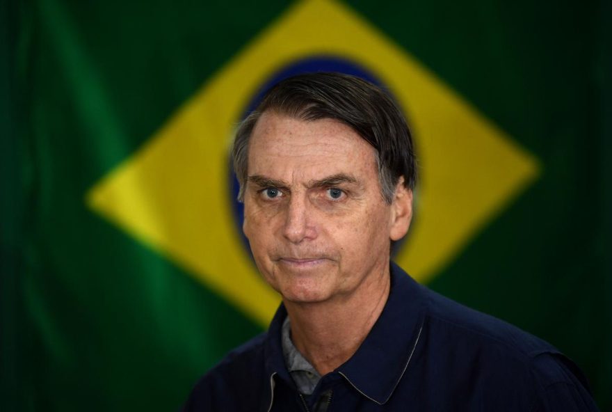 (FILES) Brazil's right-wing presidential candidate for the Social Liberal Party (PSL) Jair Bolsonaro walks in front of the Brazilian flag as he prepares to cast his vote during the general elections, in Rio de Janeiro, Brazil, on October 7, 2018. Brazil's Supreme Court on September 11, 2025, convicted firebrand ex-president Jair Bolsonaro of plotting a coup, sealing his fate with a 4-1 vote that could send him to prison for the rest of his life. All but one judge found the 70-year-old guilty of plotting to overthrow Luiz Inacio Lula da Silva following his October 2022 elections defeat by the left-winger. (Photo by Mauro PIMENTEL / AFP)