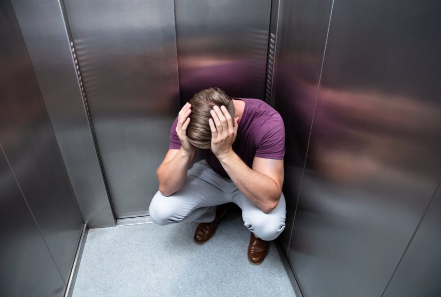 Crouched Worried Man With Hands On Head In Elevator