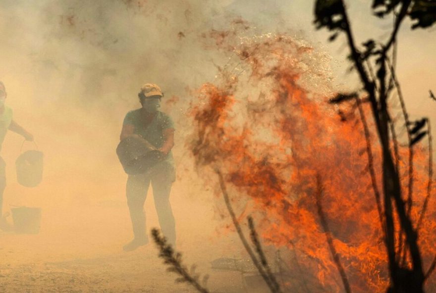 People use buckets of water to extinguish a wildfire that threatens their house in the Portuguese village of Antas, in Trancoso, on August 15, 2025. (Photo by PATRICIA DE MELO MOREIRA / AFP)