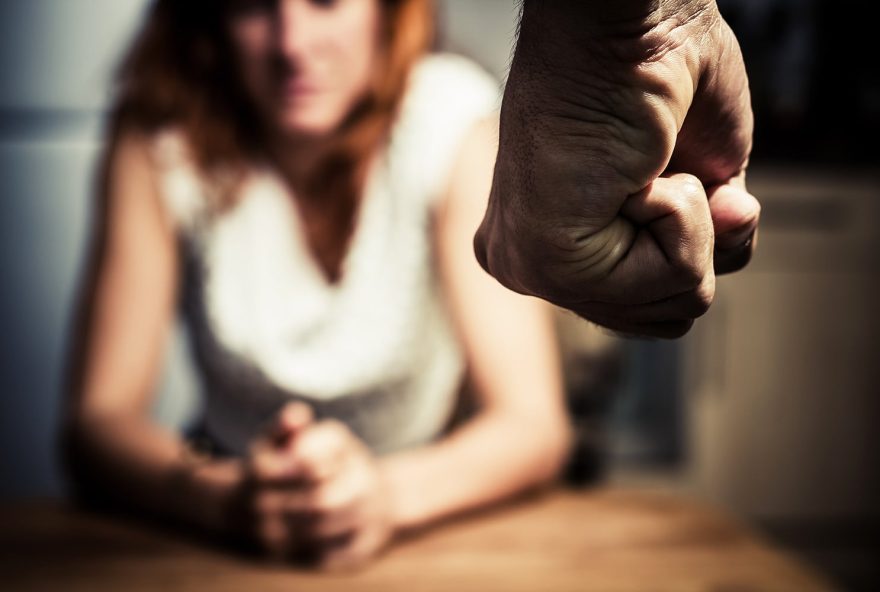 Young woman is sitting hunched at a table at home, the focus is on a man's fist in the foregound of the image